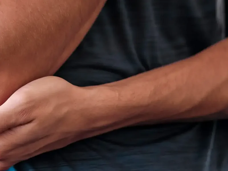 A person cradling a sore forearm and elbow, a common presentation treated at HJ Manhattan Physical Therapy