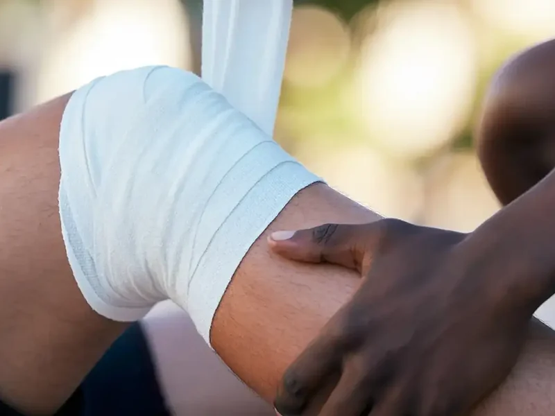 A bandaged knee being examined by hand, part of the hip and knee care at HJ Manhattan Physical Therapy