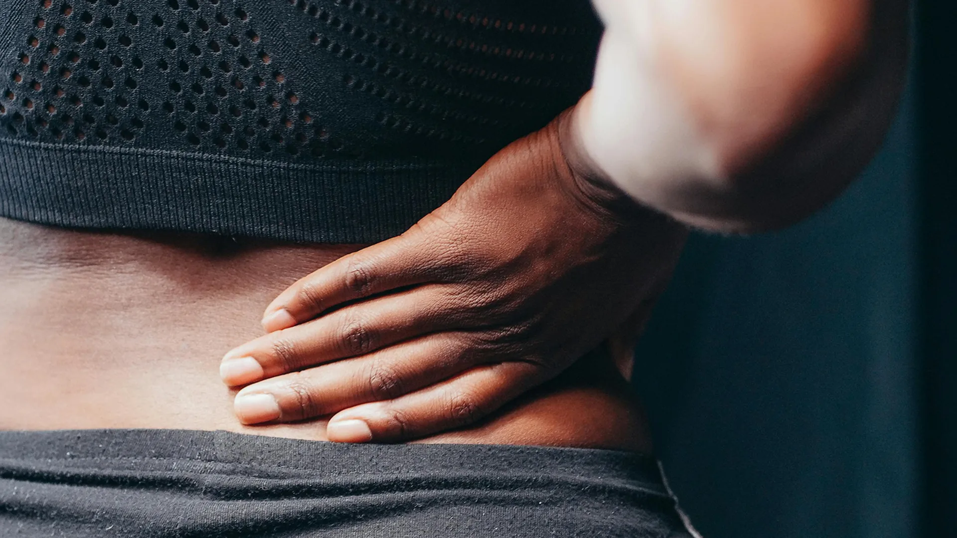 Close-up of a person pressing a hand into their lower back, the kind of lumbar pain treated at HJ Manhattan Physical Therapy in New York