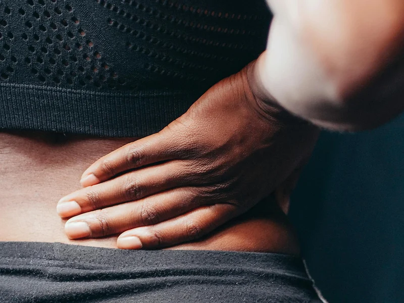 Person holding the small of their back, a common presentation of the lower back pain treated at HJ Manhattan Physical Therapy