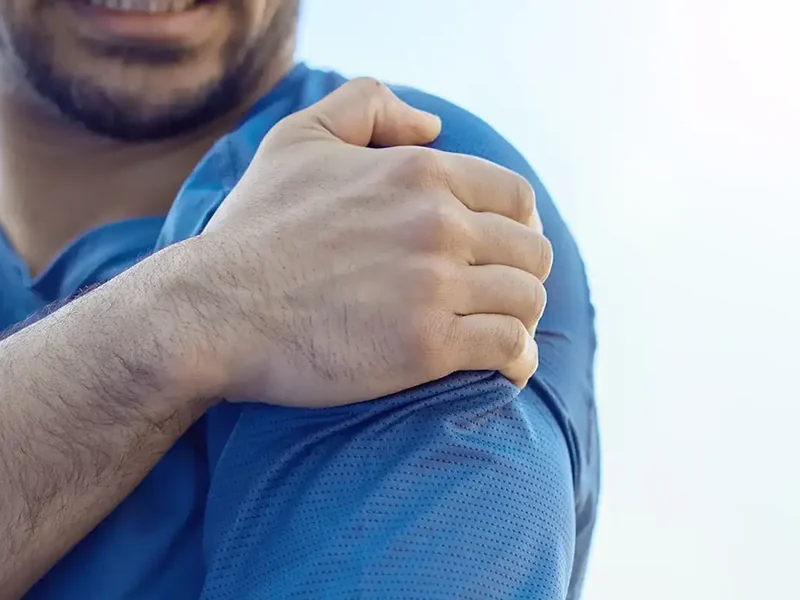 Close-up of a hand holding a sore shoulder, a common presentation treated at HJ Manhattan Physical Therapy