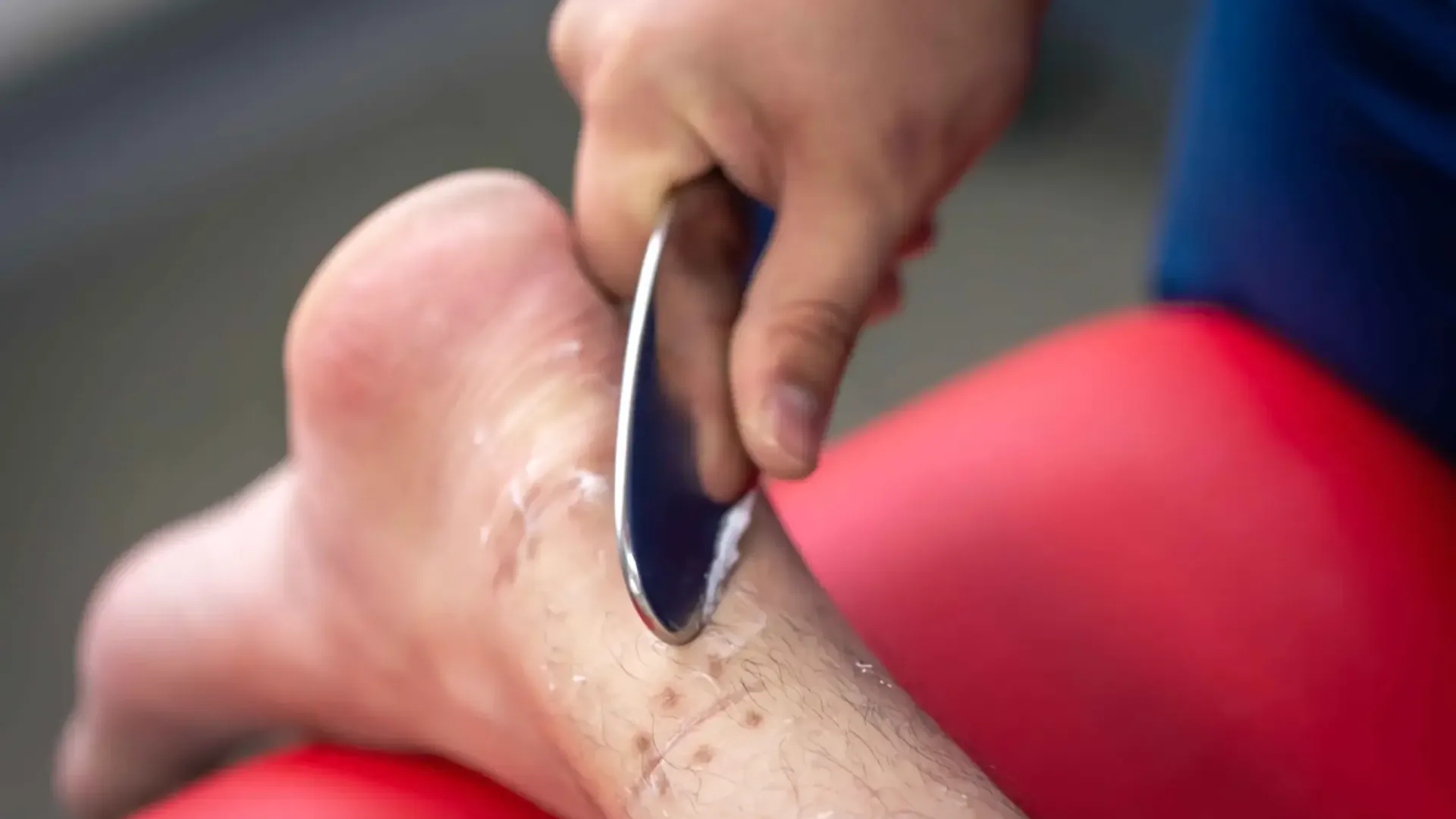 Therapist using a stainless steel IASTM tool along a patient's lower leg and ankle at HJ Manhattan Physical Therapy