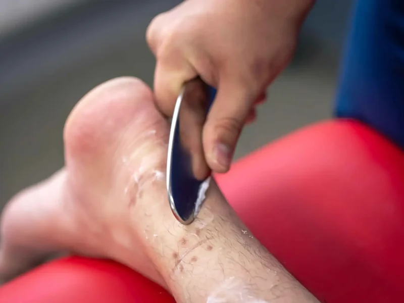 Close-up of a stainless steel soft tissue tool being drawn along a patient's shin at HJ Manhattan Physical Therapy